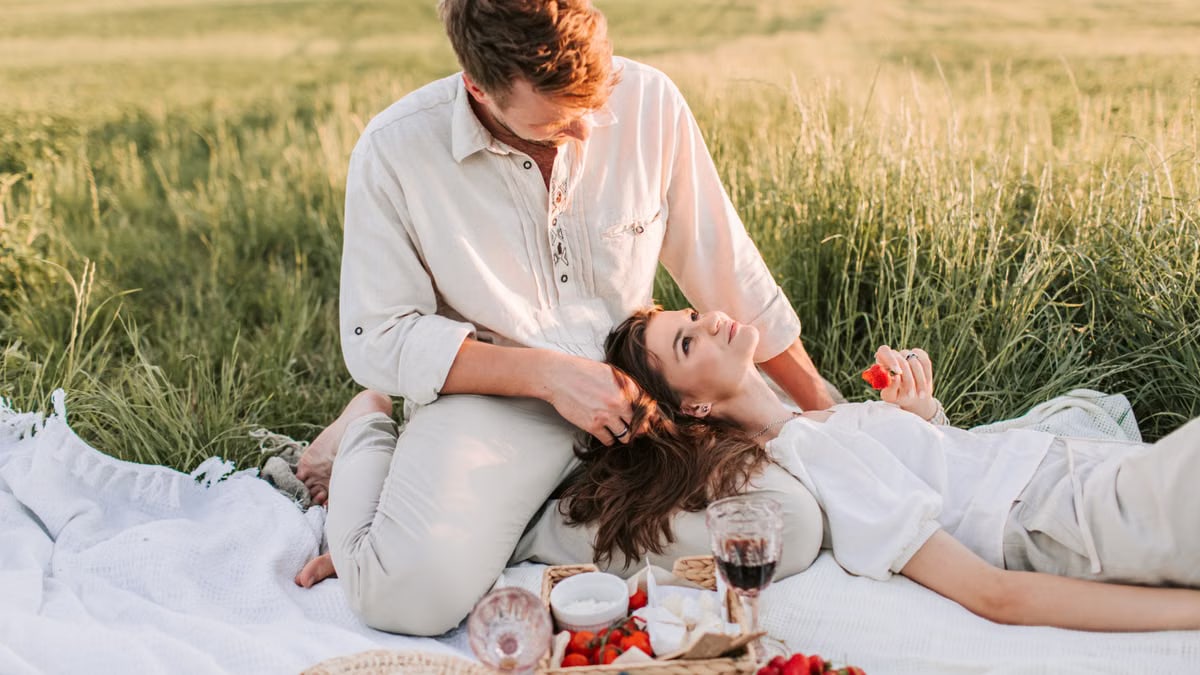 Couple enjoying a romantic picnic outdoors in lush green field, eating strawberries and blueberries.
