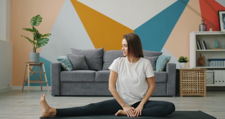 Attractive girl in leggings and T-shirt is doing stretching exercises on yoga mat relaxing on floor at home busy with practise. Youth, lifestyle and health concept.